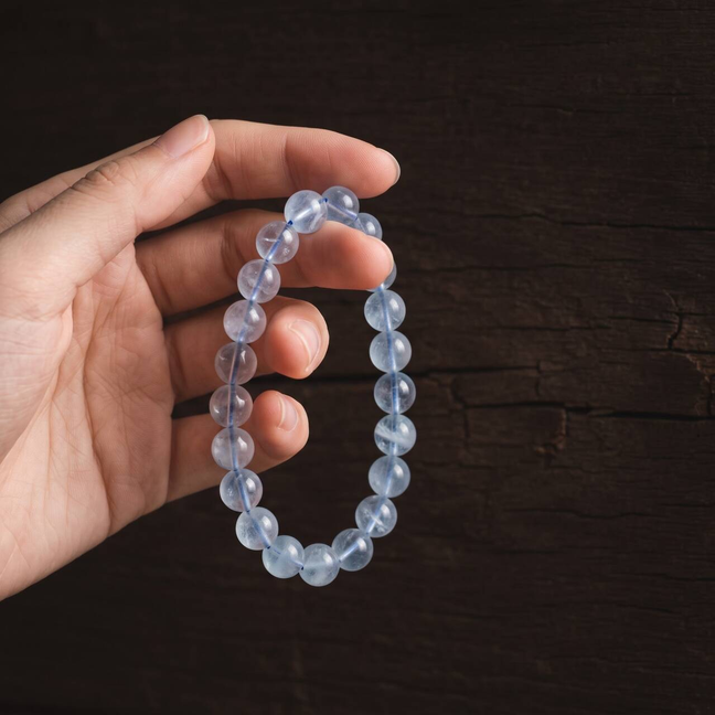 Icy pale blue 10mm aquamarine bracelet held in hand under natural light