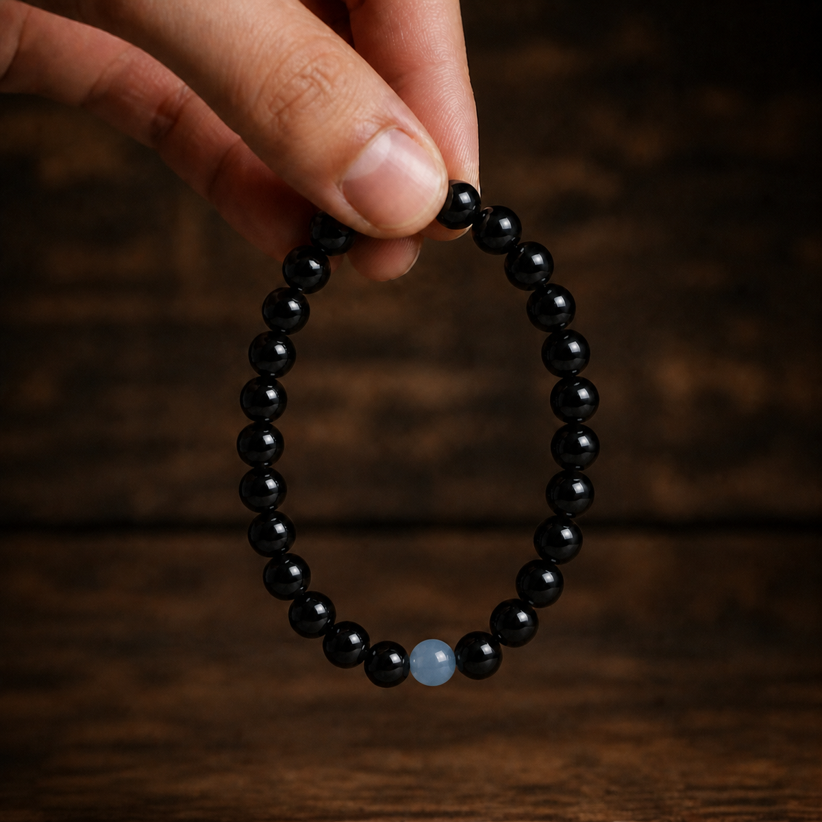 Hand holding the 7MM natural obsidian bracelet against a dark brown wood setting